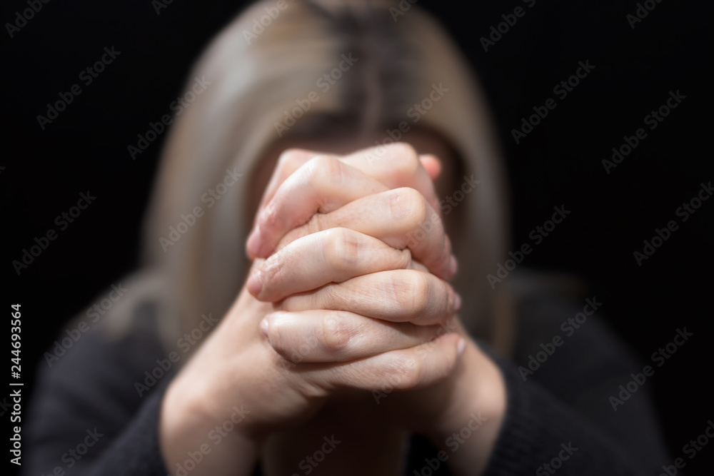 Woman praying with her hands clasped in front of her face, in dark room