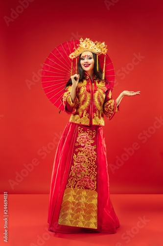 Chinese traditional graceful woman at studio over red background. Beautiful girl wearing national costume. Chinese New Year, elegance, grace, performer, performance, dance, actress, dress concept © master1305