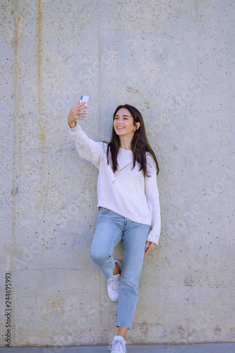 Selfie mania! Excited young girl is making a photo with smartphone. outdoors - Image