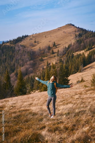 happy woman hiker standing on edge of mountain ridge against background of sunset