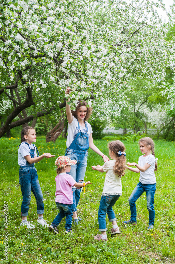 Woman and four little girls playing in blooming apple blossom garden. Family concept