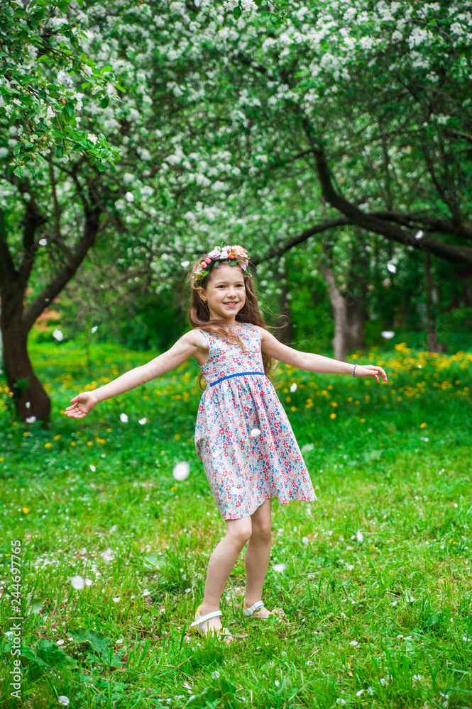 Beautiful girl dances in a flowering apple orchard under falling white petals