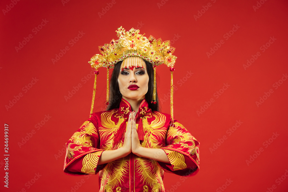 Fototapeta premium Chinese traditional graceful woman at studio over red background. Beautiful girl wearing national costume. Chinese New Year, elegance, grace, performer, performance, dance, actress, dress concept