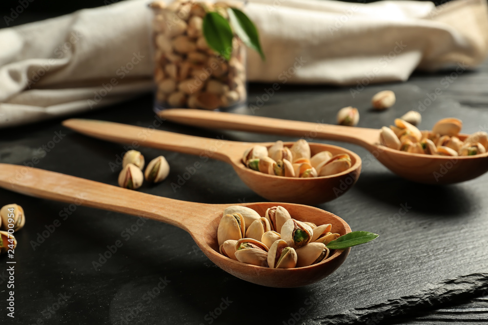 Spoons with tasty pistachio nuts on slate plate