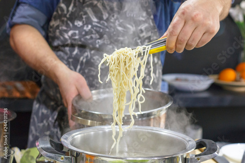 Chef takes out with slotted spoon hot steaming egg noodles from the pan