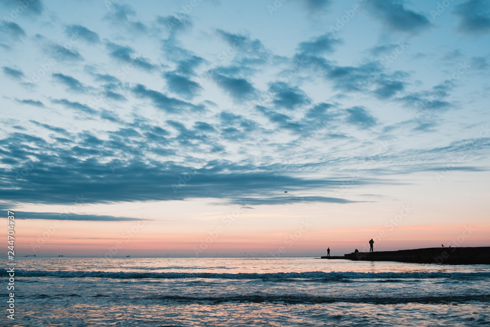 Beautiful cloudy sunrise on Black Sea shore with fisherman on dock