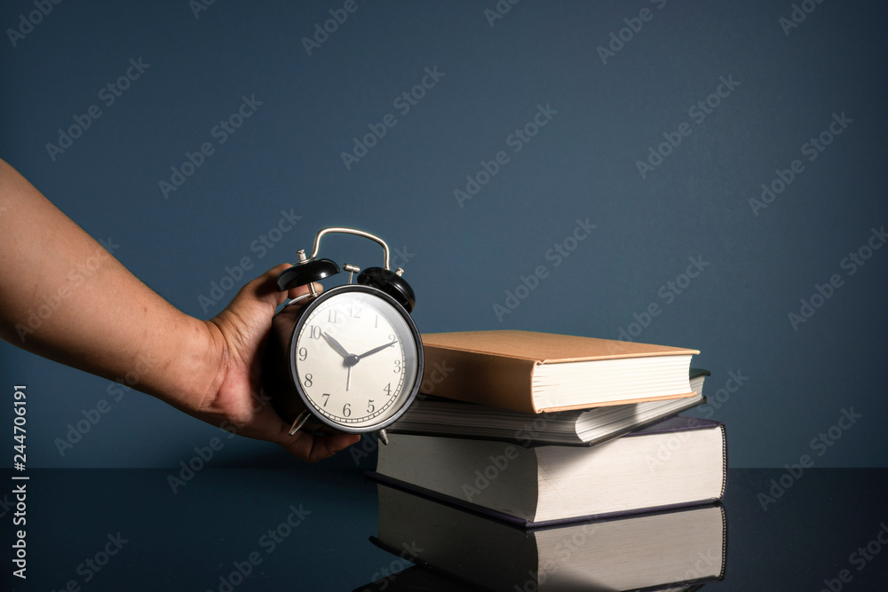 Hand holding clock and stacking books with low light Hand holding clock and stacking books with low light