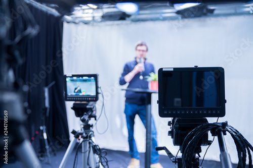 Journalist in a television studio is talking into a microphone, blurry film cameras