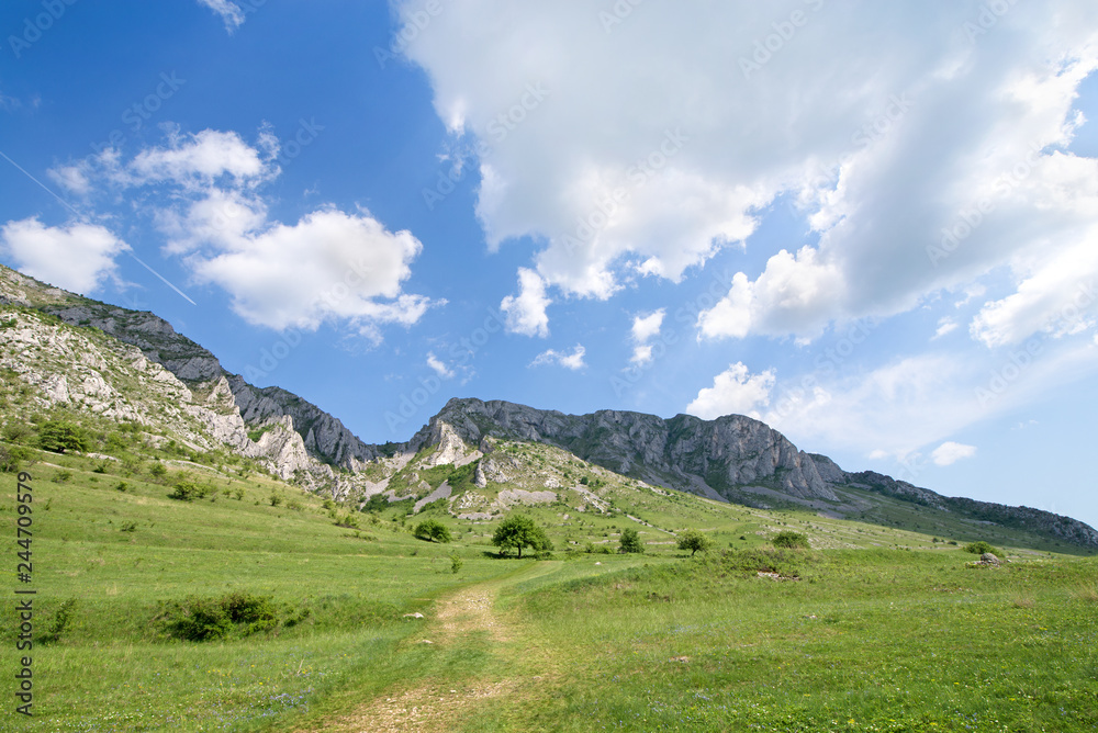 Sunny summer day, white clouds over mountain peak, where tourists climb to conquer fear, find courage and develop lateral thinking skills to overcome the difficulty of climbing a mountain. Small road 