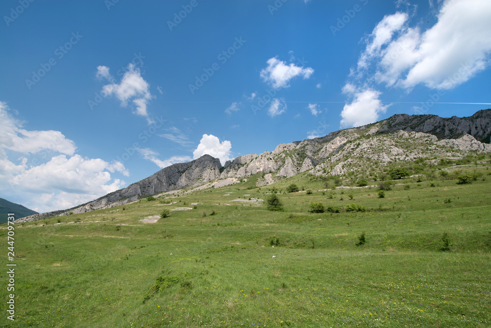 Sunny summer day, white clouds over mountain peak, where tourists climb to conquer fear, find courage and develop lateral thinking skills to overcome the difficulty of climbing a mountain. Small road 