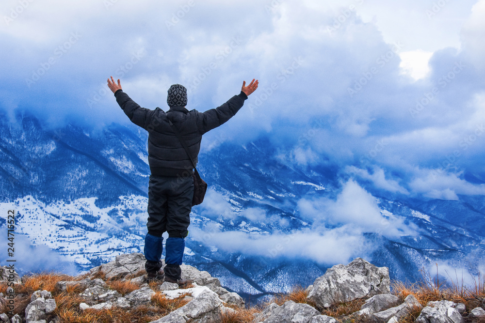 Hiker standing on a mountain top and looking into dynamic sky. Foggy mountain, Colorful winter landscape