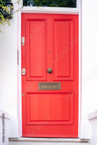 Beautiful red door with letterbox in a white house facade in Notting Hill