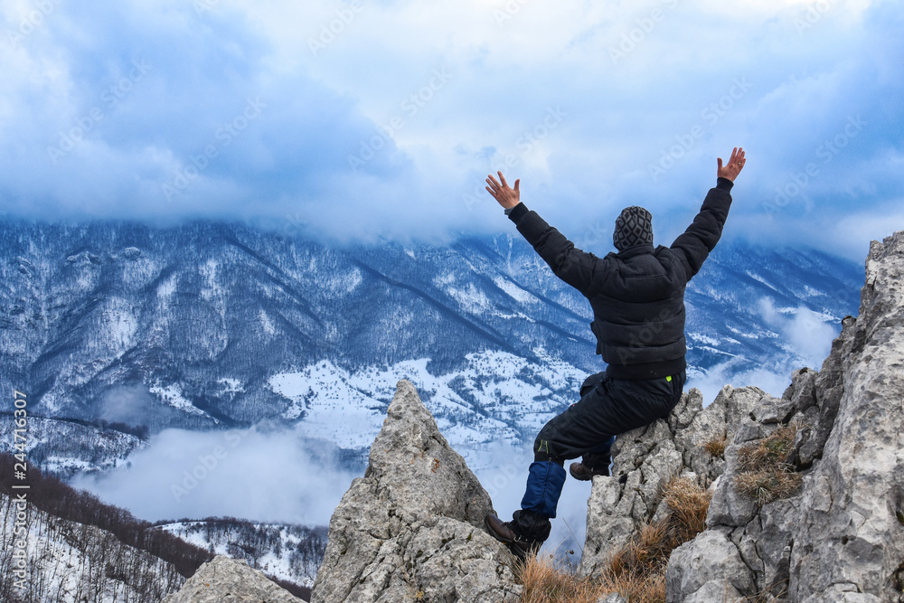 Hiker standing on a mountain top and looking into dynamic sky. Foggy mountain, Colorful winter landscape Hiker standing on a mountain top and looking into dynamic sky. Foggy mountain, Colorful winter landscape