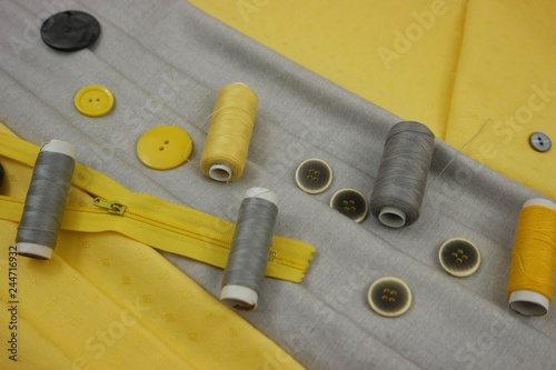 Combination of the colors at design of clothes, gray cotton fabric with yellow one. Assortment of the accessories for sewing and needlework photo