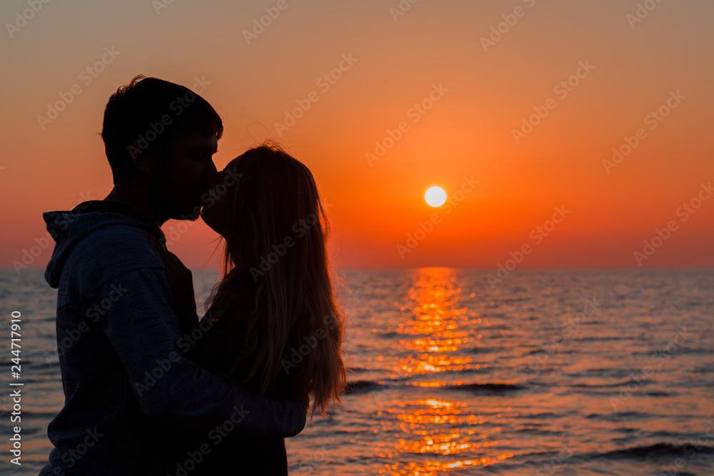 Young couple hugging each other and kissing at orange sunset. Silhouettes  on sea background. Peaceful atmosphere in summer evening. Side view.  Closeup. Photos | Adobe Stock