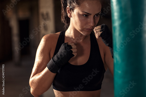 Female boxer punching a boxing bag in warehouse.