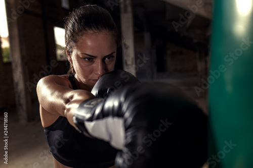 Female boxer punching a boxing bag in warehouse.