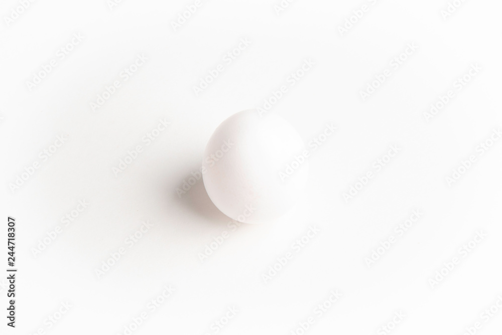 A perfectly standing raw white egg on a plain white paper background. A perfectly standing raw white egg on a plain white paper background.