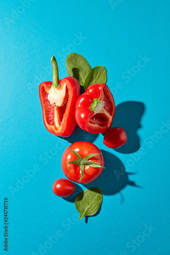 Red pepper halv, juicy tomatoes and spinach leaves with shadow reflection on a blue background with copy space. Ingredients for Salad. Flat lay photo