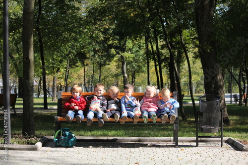 Six babies sitting in urban green nature park on the bench