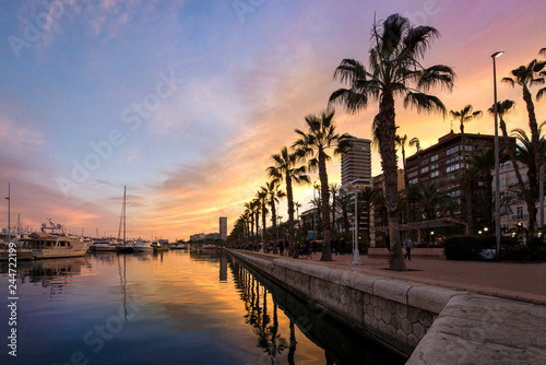 Beautiful port of Alicante, Spain at Mediterranean sea. Luxury yachts, ships, ferries and fishing boats sailing and standing in rows in harbor. Rich people traveling around the world. Sunset evening 