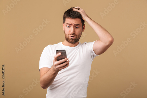 Confused young casual man holding mobile phone