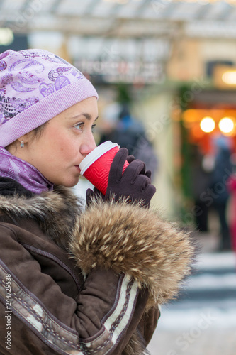 Beautiful woman drinking coffee in the street of winter clothes. Portrait Of Stylish Smiling Woman In Winter Clothes Drinking Hot Coffee. Female Winter Style. vertical photo.