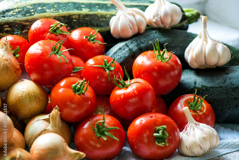Ripe fresh harvested vegetables on table. Onions, tomatoes, garlic, pepper, zucchini in kitchen. Making delicious vegetarian meal or canning veggies for winter in jars. Concept of healthy eating Ripe fresh harvested vegetables on table. Onions, tomatoes, garlic, pepper, zucchini in kitchen. Making delicious vegetarian meal or canning veggies for winter in jars. Concept of healthy eating