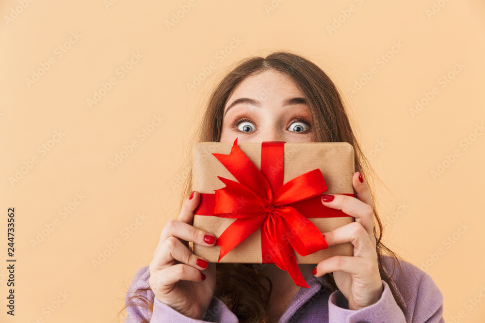 Image of surprised woman 20s with long hair smiling and holding present box, standing isolated over beige background Image of surprised woman 20s with long hair smiling and holding present box, standing isolated over beige background