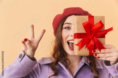 Image of birthday woman 20s with long hair smiling and holding gift box, standing isolated over beige background