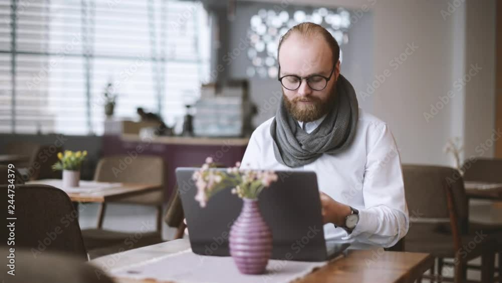 Man sitting in coffee shop talking on smartphone in front of his laptop Man sitting in coffee shop talking on smartphone in front of his laptop