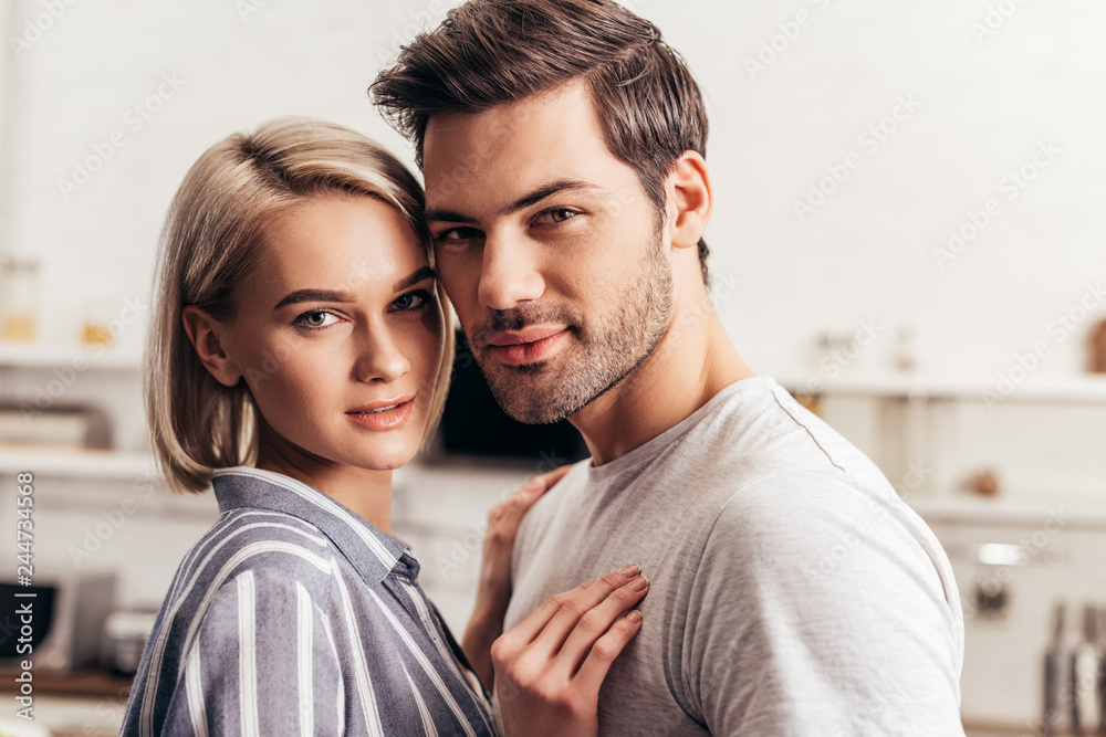 selective focus of handsome boyfriend and attractive girlfriend hugging and looking at camera selective focus of handsome boyfriend and attractive girlfriend hugging and looking at camera