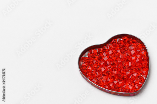 .Valentines day gray background on it a box in the form of a heart, it are glass crystals of red , scarlet, ruby color . The heart is located at the bottom right.