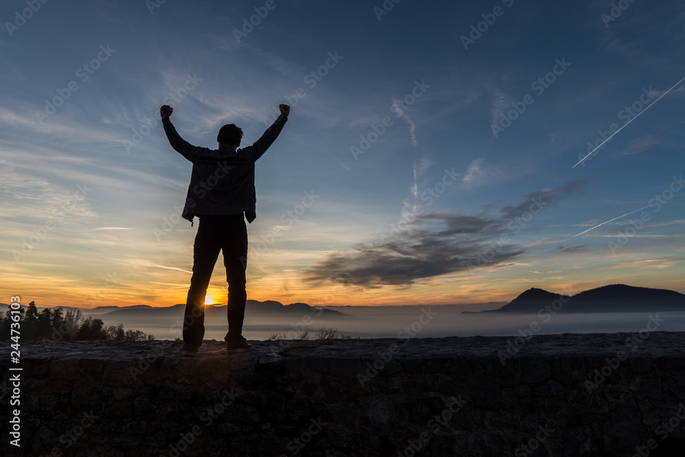 Young man standing on an old wall under glorious evening sky