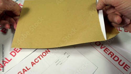 Credit crunch debt and recession. Opening an envelope marked urgent on top of many unpaid bills to reveal an invoice demanding urgent payment with the threat of legal action. photo