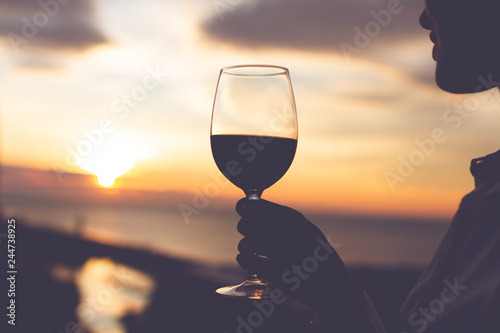 Silhouette of a young woman relaxing, enjoying and drinking a glass of wine at sunset in the evening.