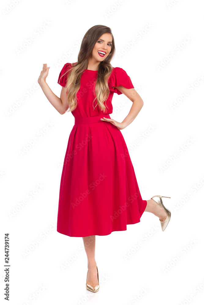 Carefree Beautiful Young Woman In Red Dress And High Heels Is Standing On One Leg And Smiling