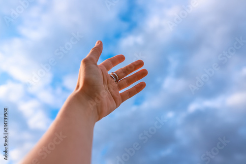 Woman's hand reaching to towards blue sky.