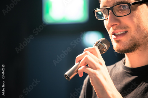 Speaker on the stage: Young Caucasian man is talking into a mirophone photo