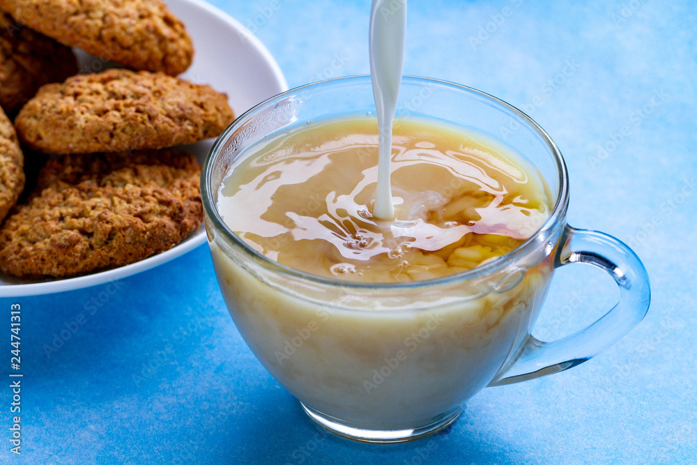 Breakfast with oatmeal cookies and pouring milk into a cup of black tea. Flour, cereal dessert and hot drink Breakfast with oatmeal cookies and pouring milk into a cup of black tea. Flour, cereal dessert and hot drink