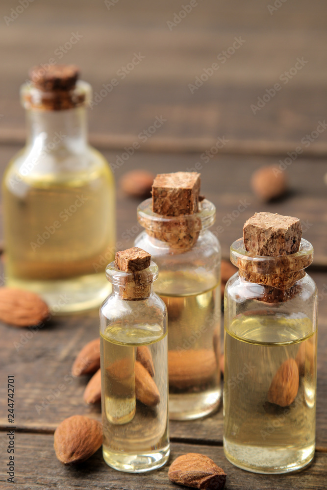 natural almond oil in a glass bottle and fresh almond nuts close-up on a brown wooden table.