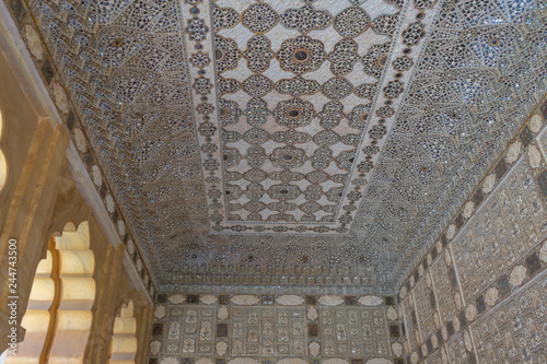 Jaipur, Rajasthan, India - April 23, 2018 : Detail of intricate mirrorwork wall is carved with beautiful paintings and flowers which was made of pure glass at heesh Mahal Garden in Amber Fort. photo