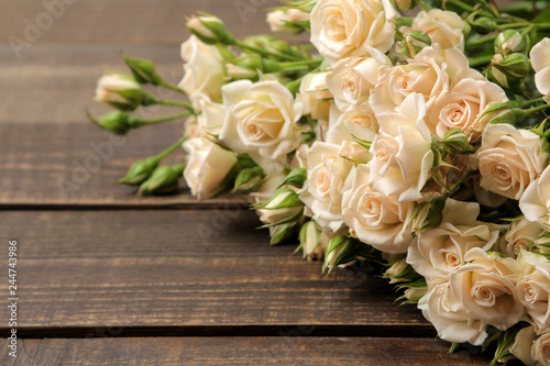 A bouquet of beautiful tender mini roses on a brown wooden table with space for text