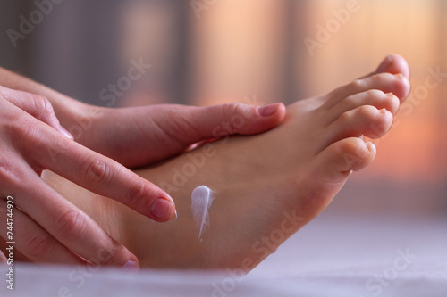 Young woman caring about her feet and applying hydrating  moisturizing cream. Foot and skin care.