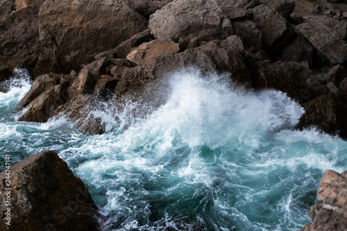 Mighty sea waves breaking on a cliff, splashing over rocks