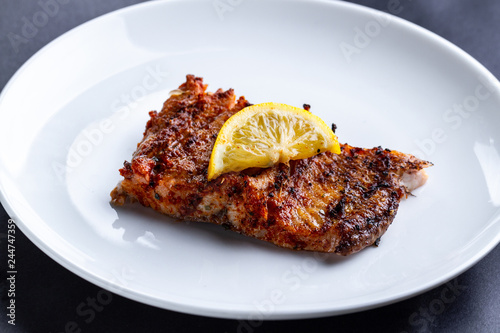Fresh, grilled salmon fillet with a slice of juicy lemon on a white plate