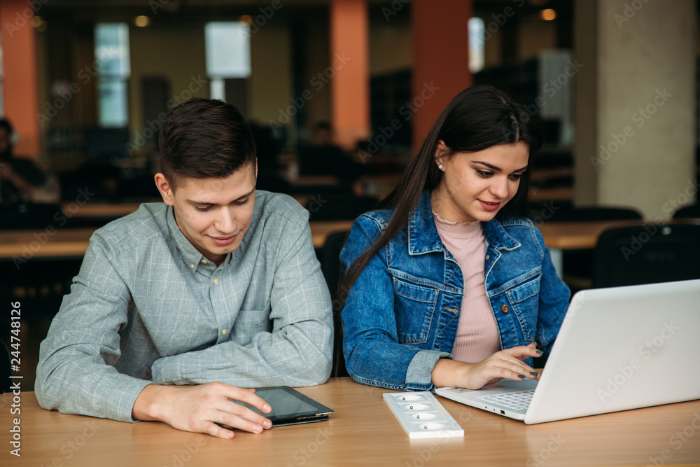 Boy and girl sits in universiti library. They use laptop to prepare for an exam. Study