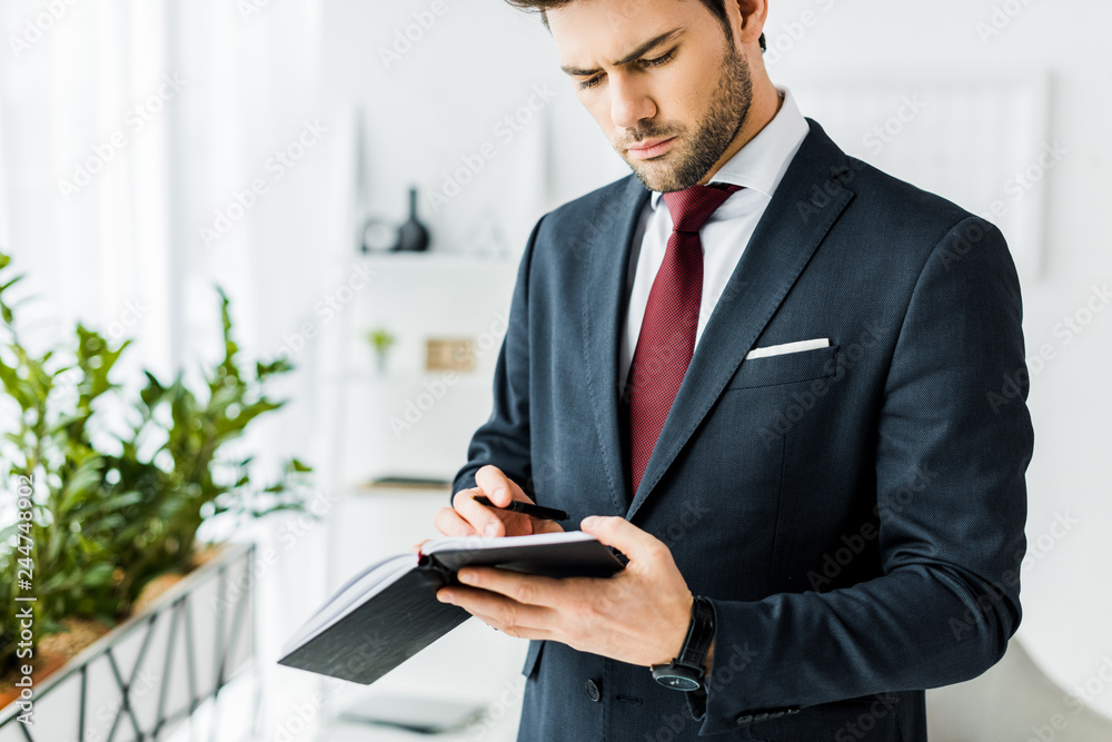 handsome businessman in formal wear writing in notebook in office handsome businessman in formal wear writing in notebook in office