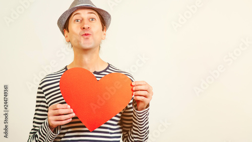 Handsome romantic guy is making airkiss. Happy Valentines Day. Funny man holding a red paper heart, on white background. Cope space. Guy holding heart postcard. photo