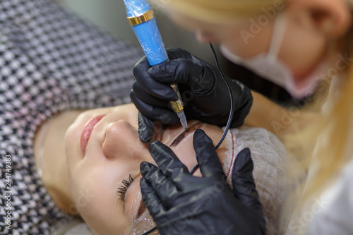 Microblading eyebrows work flow in a beauty salon. Woman having her eye brows tinted. Semi-permanent makeup for eyebrows. Focus on model's face and eyebrow photo